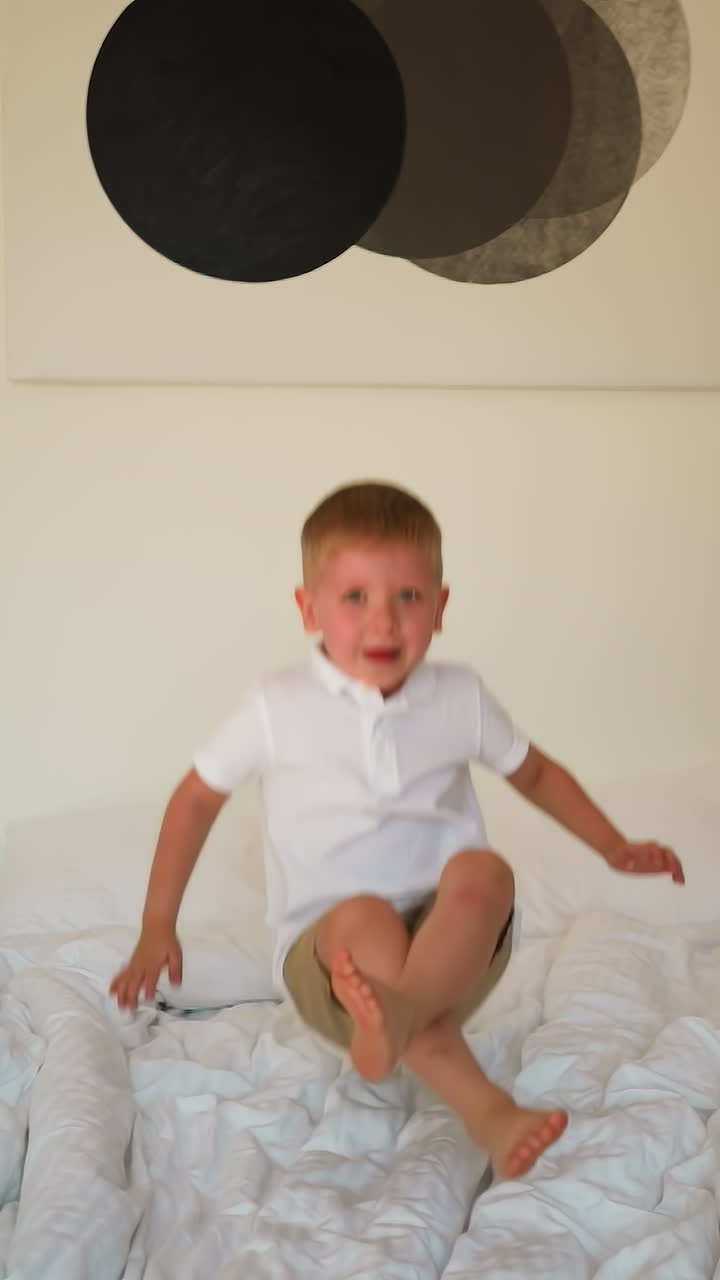 귀여운 소년은 밝은 색의 린으로 침대에 뛰어들어, 유쾌한 유아는 현대적인 가운 침실에서 부드러운 침대에 뛰어다니며 좋은 시간을 보내고, 행복한 어린 시절의 순간.