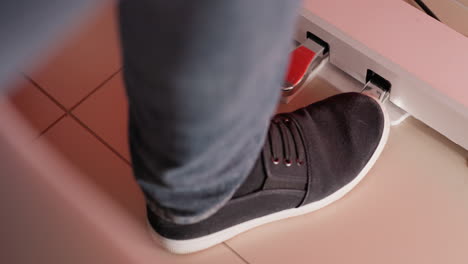 a foot wearing a black shoe and blue jeans gently tapping on a piano pedal. the scene is highlighted by a soft red hue in the background, adding warmth and depth