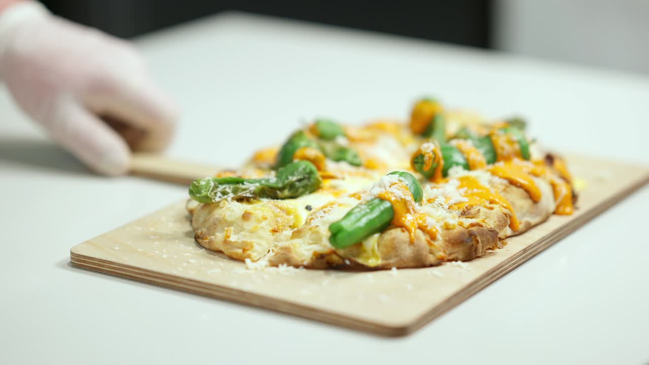 카메라는 피자 조리판과 함께 나무로 된 절단판을 따라 다니며 남성 손으로 테이블 위에 페이스트리를 밀고 있습니다. 알 수 없는 남성 백인 요리사는 피자 가게 부에서 맛있는 음식을 보여줍니다.