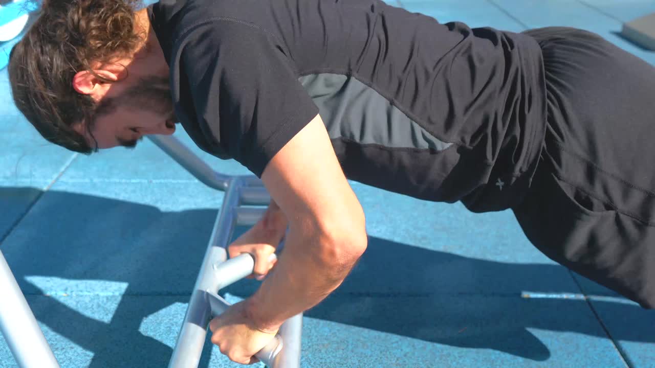 Hispanic man with pony tail does diamond push ups on bars at outdoor fitness course, close up