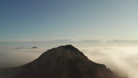 fog swirling around silhouette mountain, aerial birds eye view above clouds