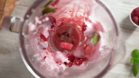 batido de yogur rosa frambuesa con hoja de menta mezclado en una licuadora de vidrio en cámara lenta, vista de arriba, dentro del dispositivo