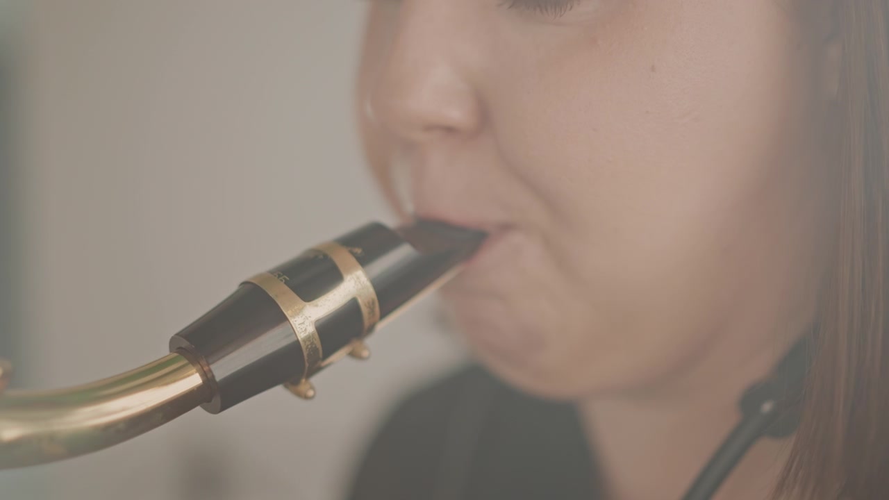 Close-up van een saxofoonmondstuk embouchure oefening, student concentreert zich tijdens privéles, instructeur coacht buiten beeld, warm studiolicht, subtiele riettrilling, ademhalingsoefeningen, gefocust.