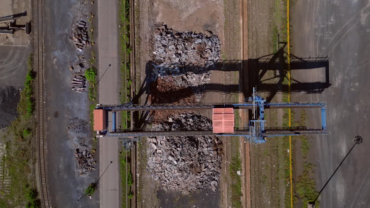 Gantry crane transporting scrap metal at Hennigsdorf electric steel mills on a sunny summer day. Unbelievable aerial view flight drone camera pointing down