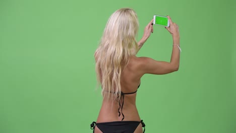 happy young beautiful blonde woman wearing bikini while taking pictures with phone