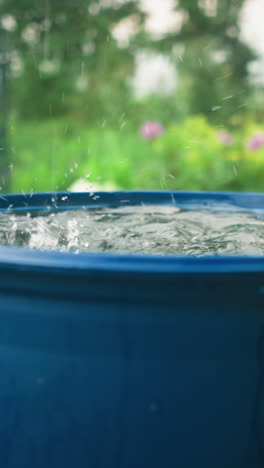 las gotas de agua en el tambor de agua azul, creando salpicaduras a medida que se forman ondas, el fondo del jardín presenta vegetación borrosa, flores coloridas y escena al aire libre