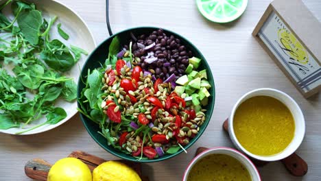 Top-view-aerial-shot-of-salad-on-platform-black-beans-lemons-pumpkin-seeds-avocado-tomatoes-leaf-spinach-dressing