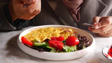 person eating an omelette with salad and tea