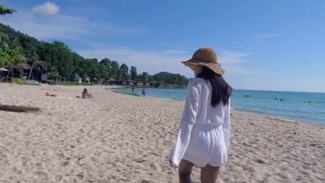 Mujer-Con-Vestido-Blanco-Y-Sombrero-Marrón-Camina-En-Una-Hermosa-Playa-De-Arena