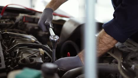 Car-mechanic-using-wrench-to-repair-the-engine-in-a-car-service,-slow-motion