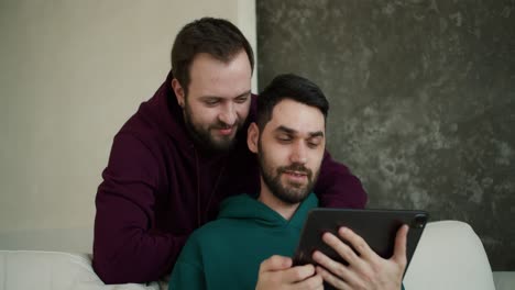 Fröhliche-Kaukasische-Männer-Schauen-Sich-Videos-Auf-Einem-Digitalen-Tablet-An,-Zeigen-Auf-Den-Bildschirm-Und-Lächeln