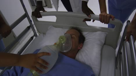 diverse group of doctors in face masks pushing patient with oxygen mask in bed in hospital corridor