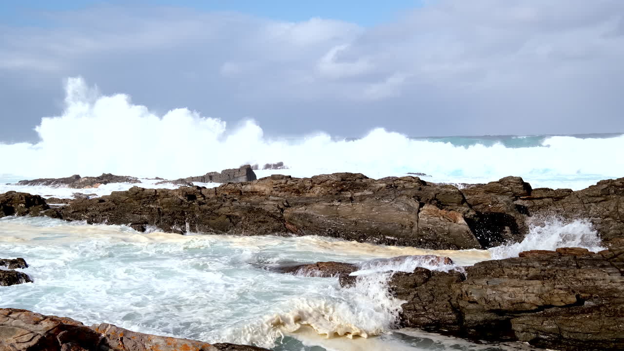 Foaming breakers crash over shallow rugged reef at Storms River mouth. Slomo