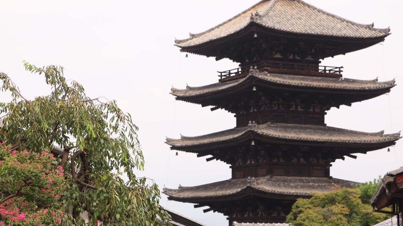 Telefoto af Yasaka Pagoden, der rejser sig over traditionelle hustage og grønne områder i Kyotos historiske Higashiyama-distrikt, og viser et af Japans ikoniske femetagers tempelvartegn