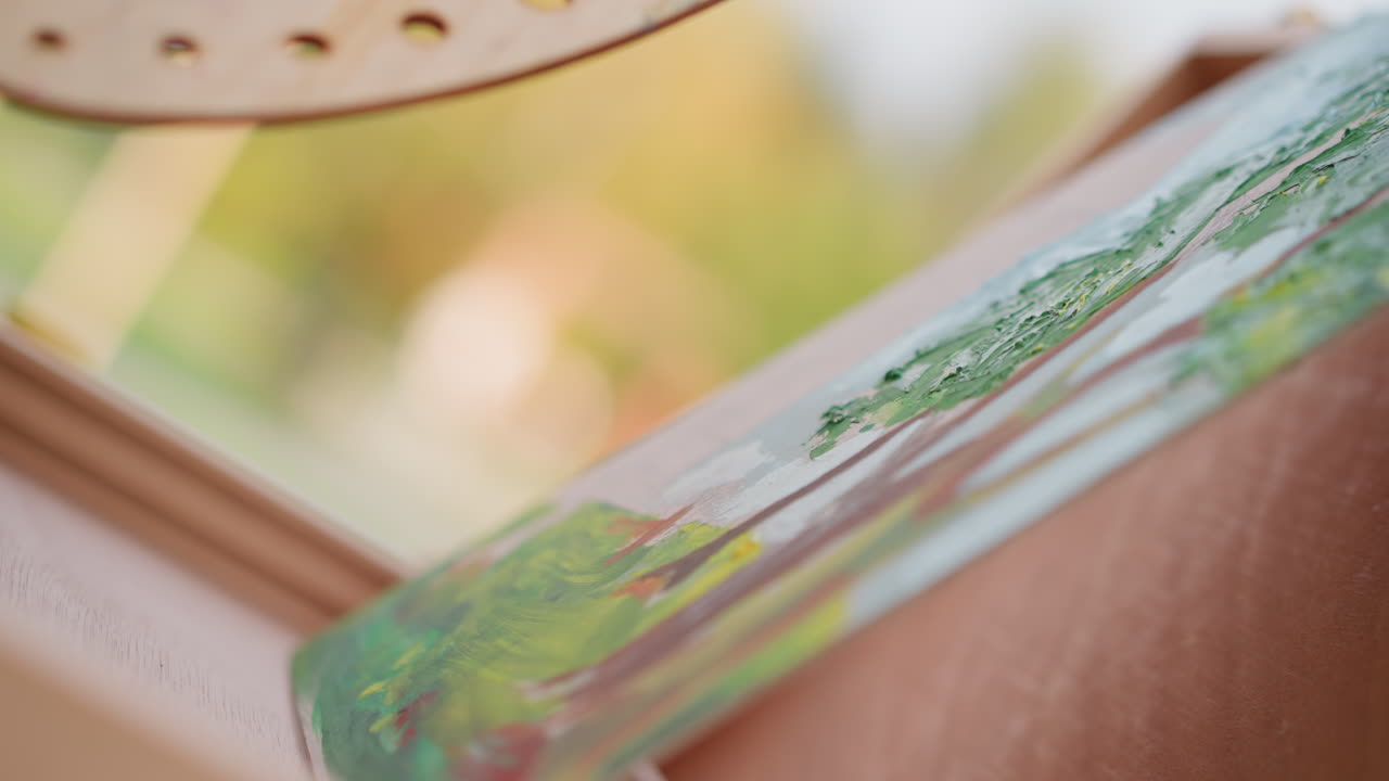 Håndpenselmaleri udendørs grønne strøg hvid, kunstner der maler et lille landskabsstudie på lærredskant, våde akryllag, levende grøn blanding, solbeskinnet park bokeh, afslappet gadekunstproces, detaljeret