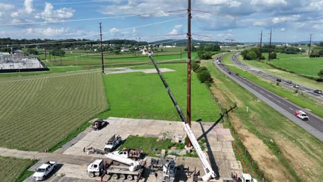 aerial view of crane with bucket lift and working linemen over countryside farm fields