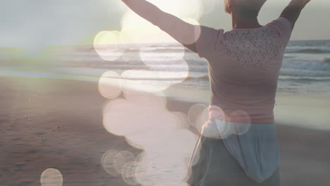 animation of light spots over caucasian woman with arms outstretched on beach