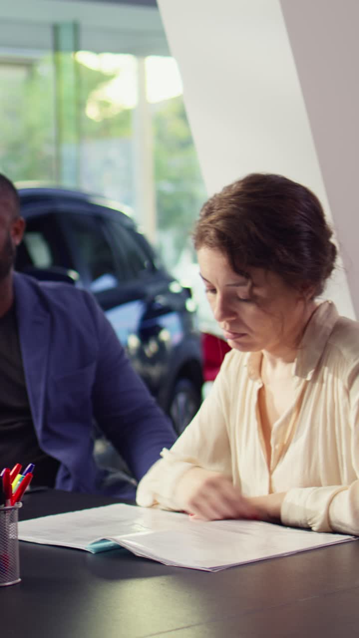 Donna e uomo che esaminano documenti in una concessionaria d'auto.