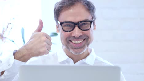 pulgares hacia arriba por un hombre de mediana edad trabajando en una computadora portátil, de cerca