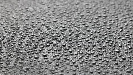 spinning closeup background of black hydrophobic fabric covered with water drops
