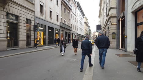 slow-motion shot of two girls with masks walking in via monte napoleone, in the late afternoon during a grey day in milan, italy.