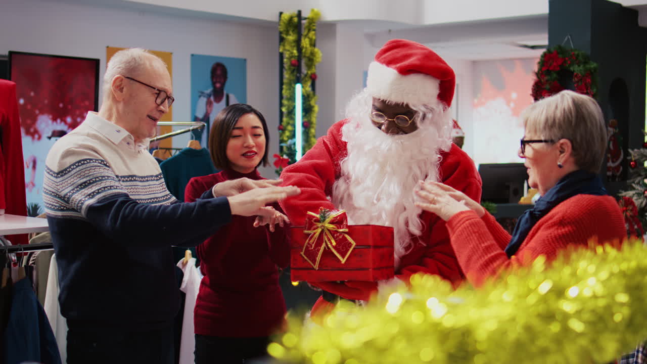 Assistente de loja vestindo fantasia de Papai Noel em uma loja de roupas com decoração natalina, segurando uma caixa de presente que funciona como recipiente de bilhetes de rifa, sorteando uma mulher asiática aleatória como vencedora entre clientes animados.