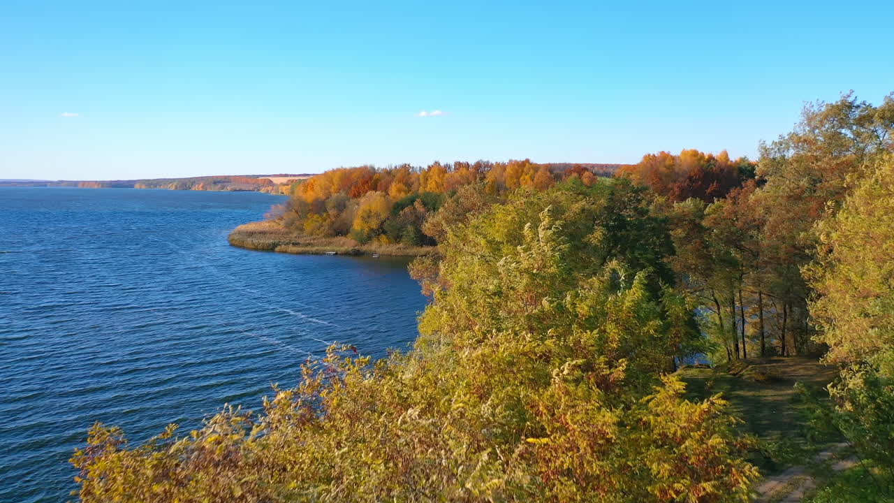Several green tree tops among the variety of colors. Path in the woods that leads to the waterfront. Birds eye view.