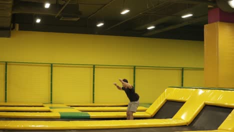 young attractive sportive athlete performs front somersaults and body twistsat professional trampoline for training.