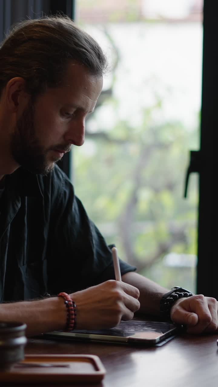 Man drawing on a tablet by the window