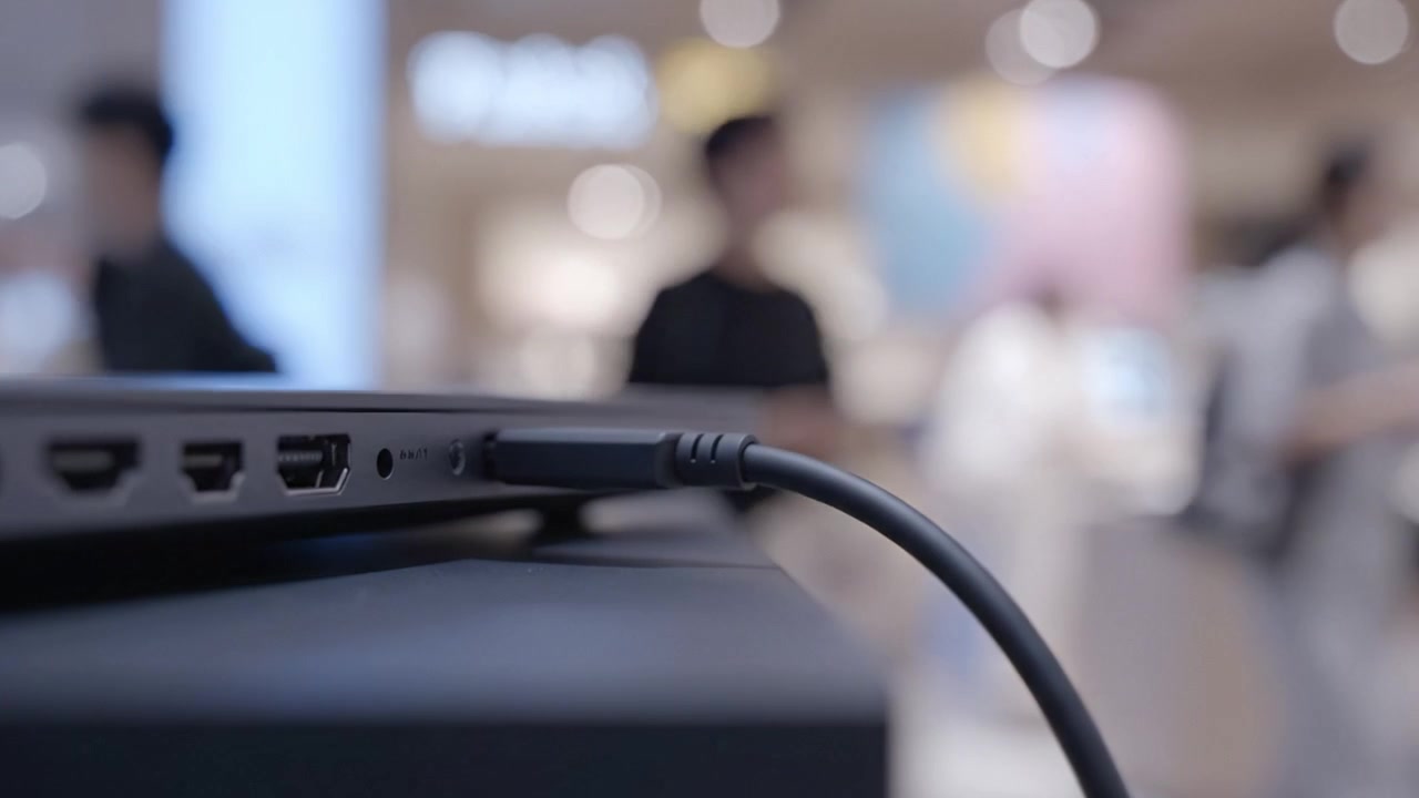 A Close-up Look at a Laptop's Ports and Connections in a Modern Retail Environment with Blurred Background Elements Indicating a Busy Store Atmosphere