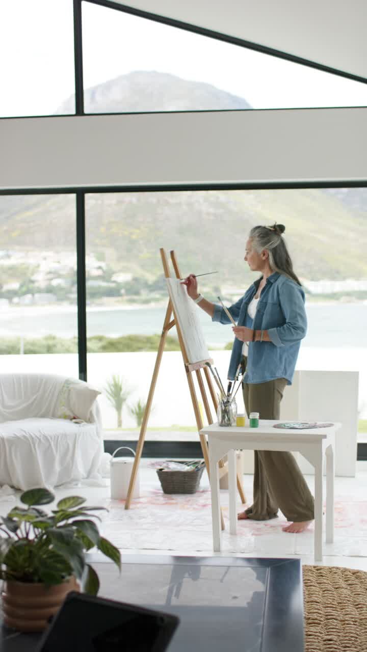 Video verticale: Un artista entra in studio, intinge il pennello nella pittura verde e dipinge la vista sul lago