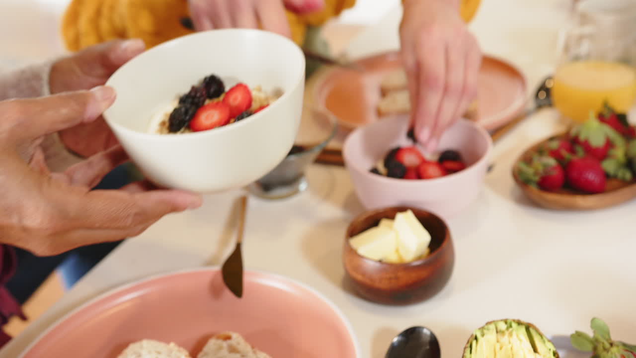 Eating breakfast together, multiracial senior couple enjoying fresh fruit and bread at home