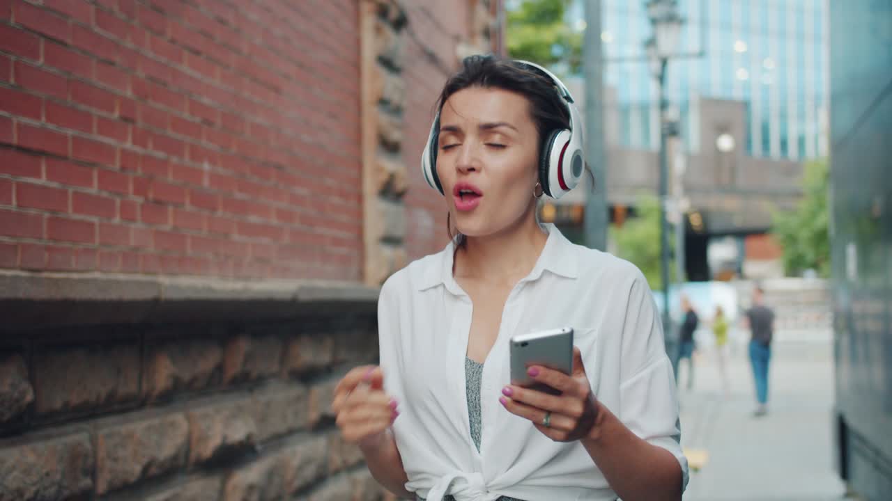 Pretty woman listening to music in headphone singing using smartphone outdoors