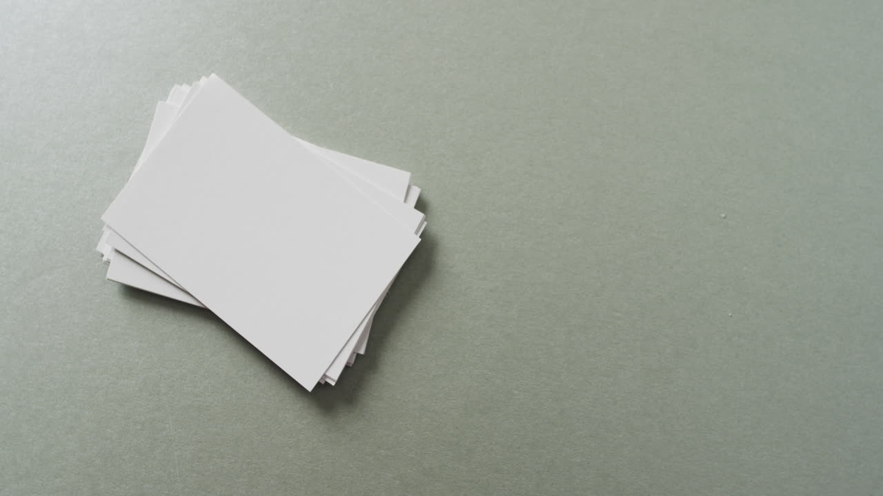 Overhead view of stack of blank white business cards on grey background, copy space, slow motion