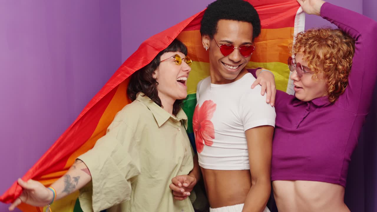 Three people posing with a rainbow flag