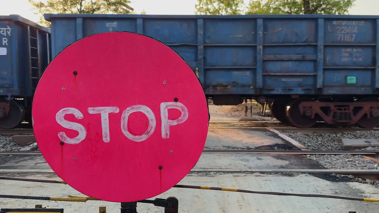 Segnale di stop ferroviario rosso brillante a un passaggio a livello con un treno merci in movimento sullo sfondo, che evidenzia la sicurezza ferroviaria, il trasporto e il controllo del traffico.