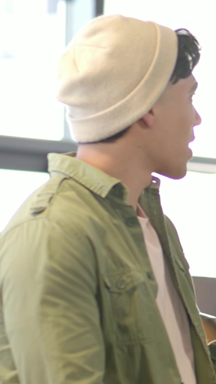Video verticale: Uomo con berretto color crema e camicia verde oliva che parla vicino alla finestra, sentendo un segnale fuori campo.