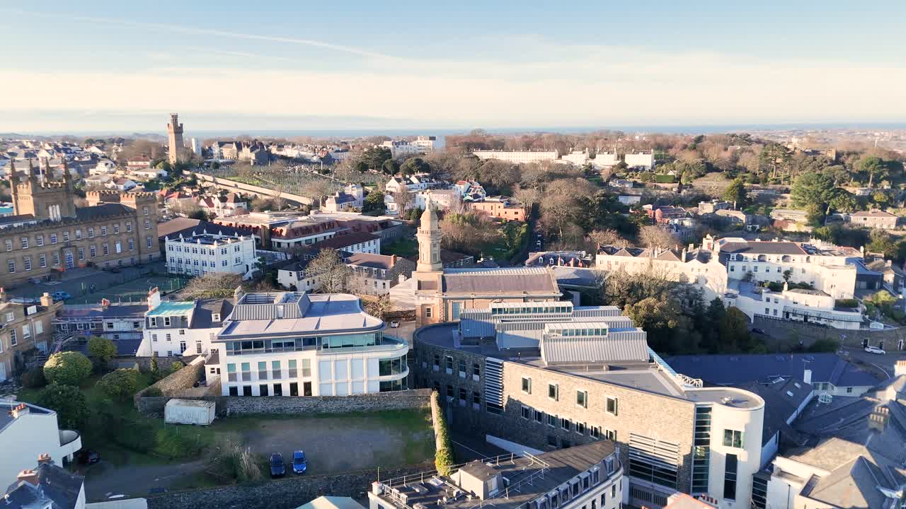 Guernsey St Peter Port.Overhead rising reveal over the roof tops of town centering on St James Assembly Hall with distant views over town out to sea on sunny afternoon.