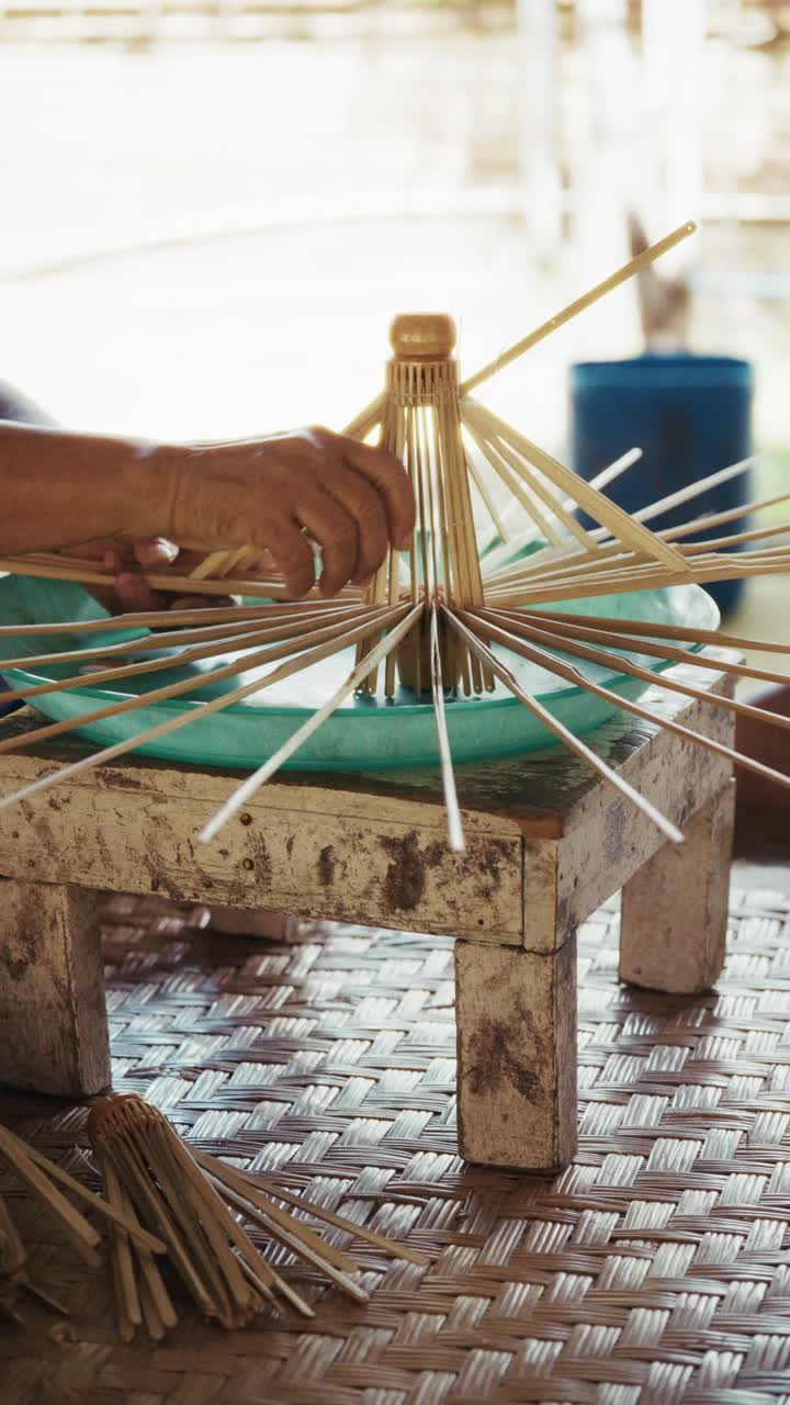 Manos artesanas montando un paraguas de papel hecho a mano, dando forma a las varillas de bambú en una mesa de trabajo sencilla dentro de un taller tradicional. Un proceso artesanal lento y preciso y una producción manual.