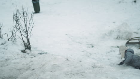 joven se desliza por la colina de nieve en el estómago, vista en cámara lenta desde atrás