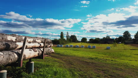 Rollos-De-Ensilaje-Y-Pila-De-Troncos-De-Pino-En-El-Patio-Trasero-De-La-Granja-En-Un-Día-Soleado-De-Verano-Con-Cielo-Azul