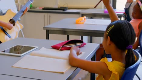 Schulkinder-Heben-Die-Hand,-Während-Sie-In-Der-Grundschule-Am-Schreibtisch-Sitzen,-4k