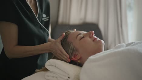 Mujer-Joven-Que-Recibe-Un-Masaje-Relajante-En-La-Cabeza-Acostada-Con-Luz-Natural