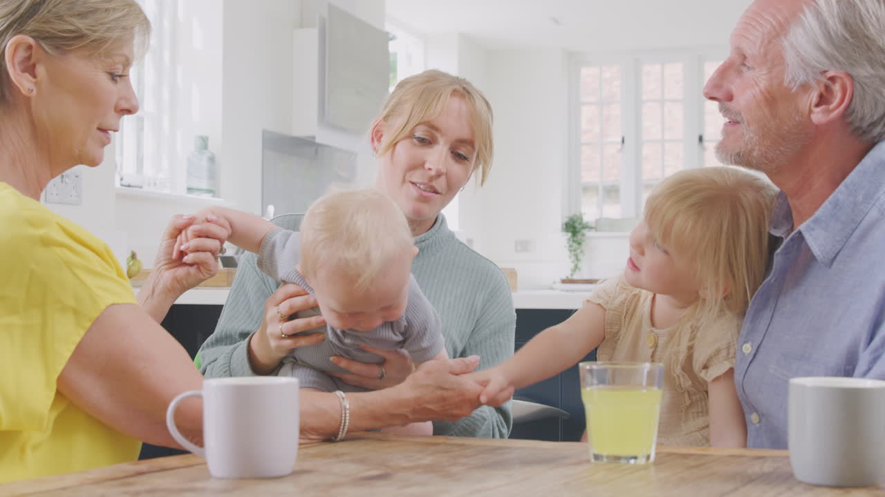 бабушки и дедушки с взрослой дочерью и внуками сидят за кухонным столом дома