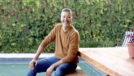 smiling man sitting by pool, enjoying outdoor leisure time, wearing casual clothes