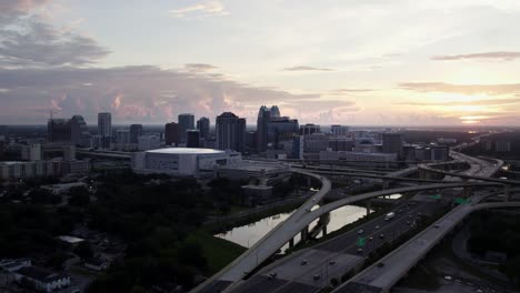 Aufsteigende-Drohnenaufnahme-Der-Innenstadt-Von-Orlando-Bei-Sonnenaufgang,-Interstate-4-Und-SR-408-Im-Vordergrund