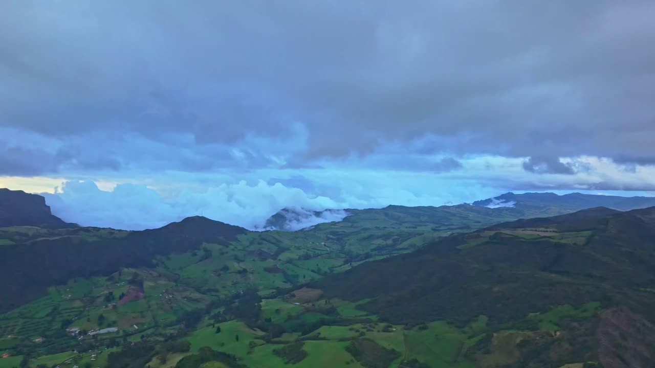 Aerial panning shot over the mountains surrounding Zipaquirá, showing clouds drifting across high ridges and green valleys under a dramatic sky