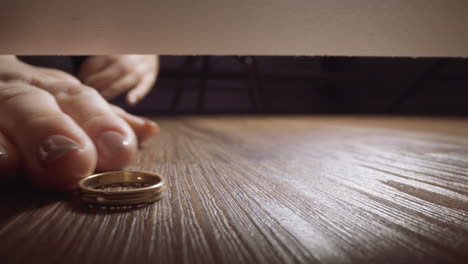 woman drops and tries to take out gold ring from under sofa