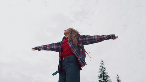 woman standing against cloudy sky in forest. female hiker raising hands