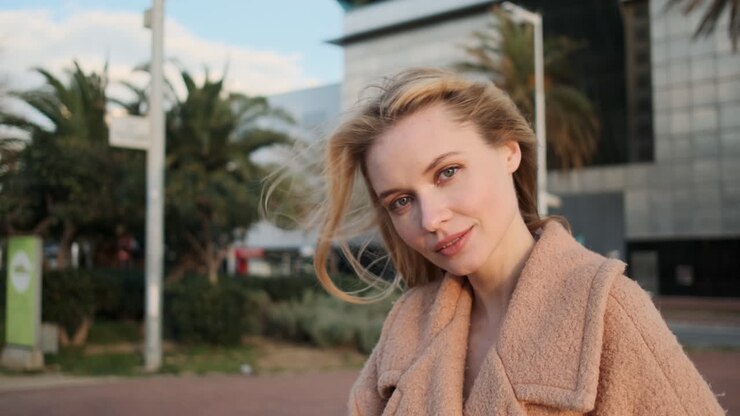 une femme blonde qui regarde la caméra à l'extérieur.